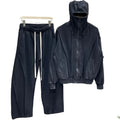 Bărbat purtând un compleu streetwear din 100% bumbac, de culoare negru spălat, format dintr-un hanorac avangardist cu glugă tip cagulă și pantaloni largi prevăzuți cu un șiret negru, lung și asimetric în talie.