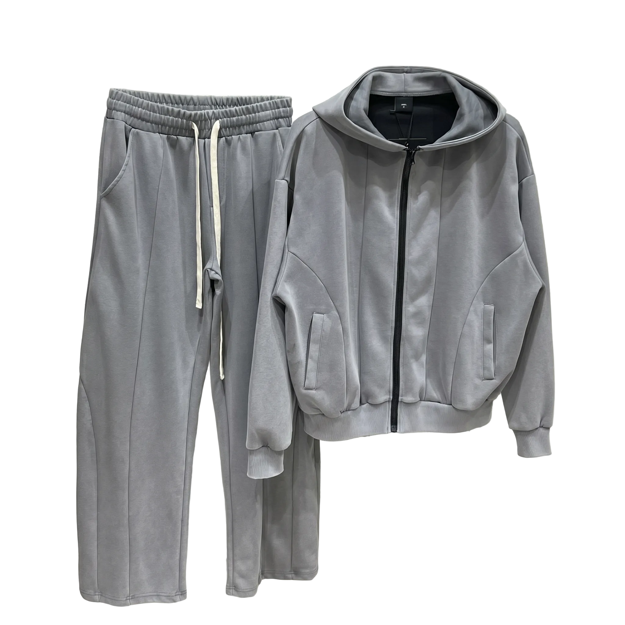 Bărbat purtând un set minimalist streetwear, format din hanorac cu fermoar și cusături arhitecturale vizibile, fără șiret la glugă, asortat cu pantaloni largi wide leg care au un șiret alb, lung și supradimensionat în talie