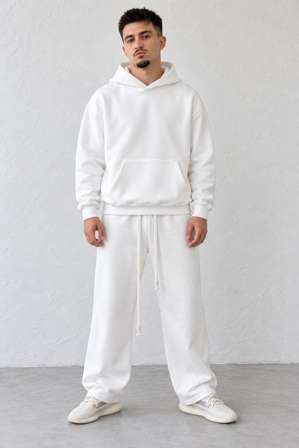 Trening alb pe model, cu hanorac fără șnur la glugă și pantaloni drepți cu șnururi lungi.