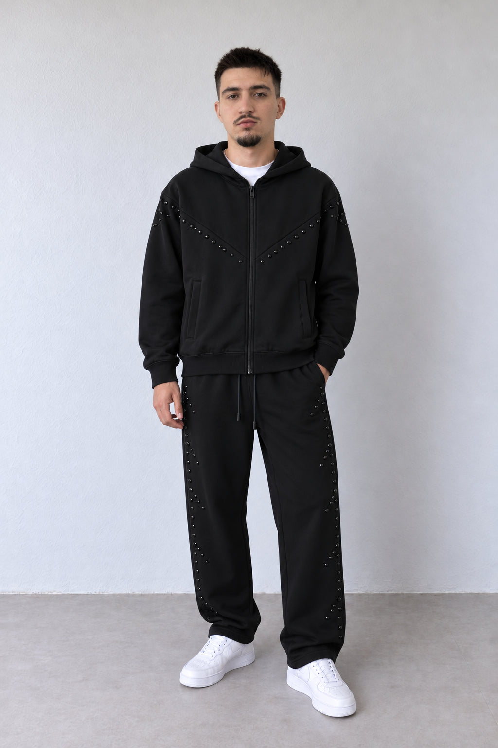 Trening negru pentru bărbați cu fermoar și aplicații tonale, ținută integrală pe model cu pantaloni asortați și sneakers albi.