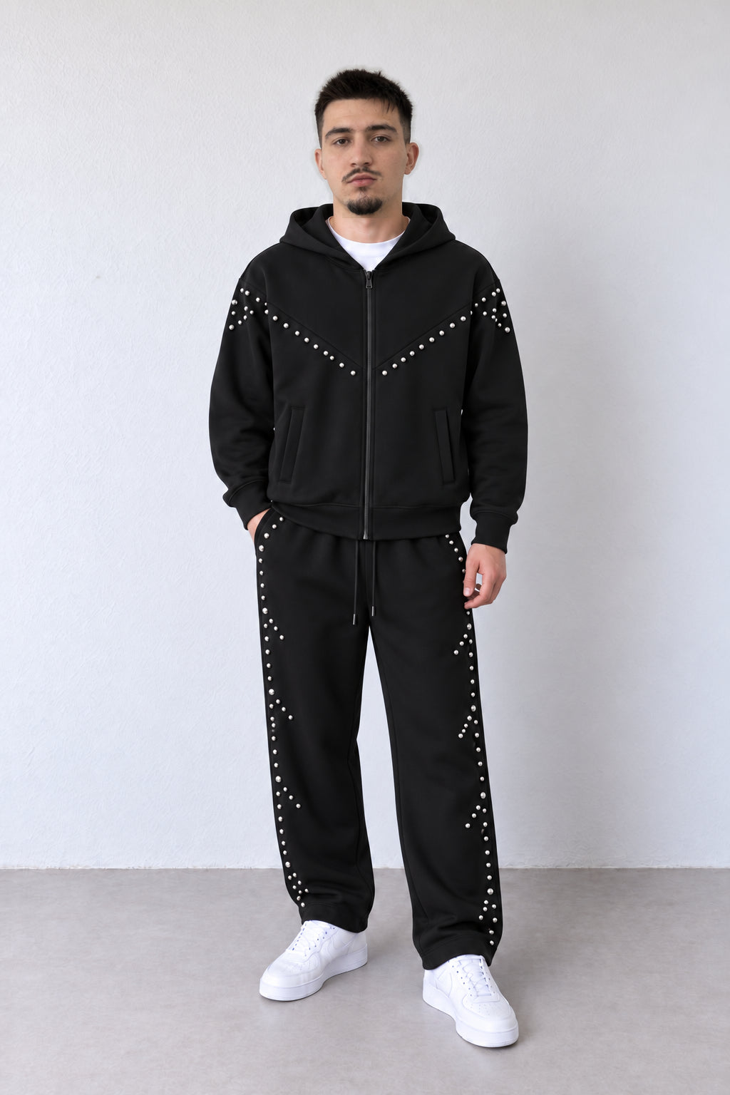 Trening negru pentru bărbați cu fermoar și capse argintii, ținută pe model în postură alternativă, cu croiala pantalonilor și aplicațiile vizibile.
