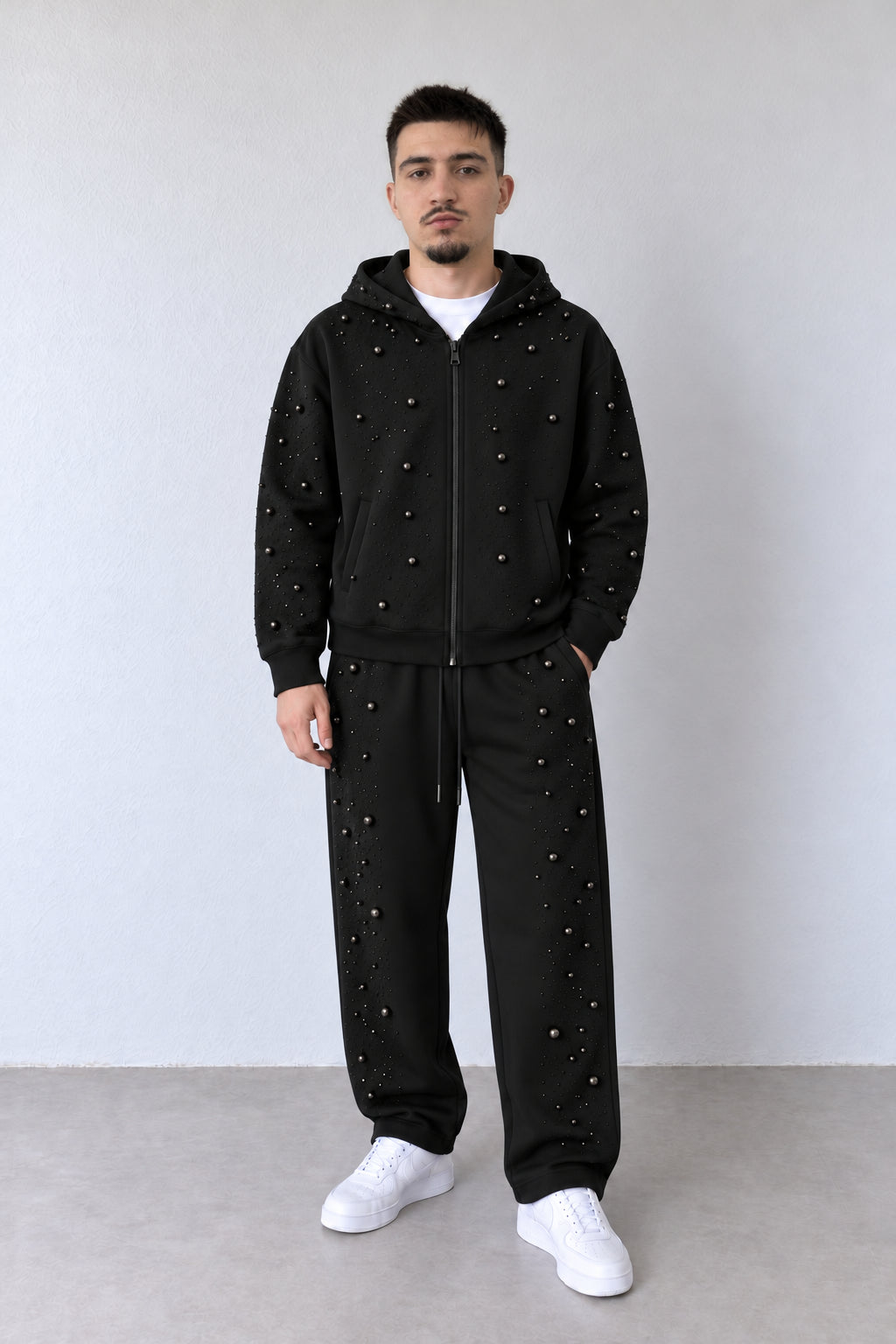 Trening negru pentru bărbați cu strasuri și mărgele decorative, ținută pe model în postură alternativă, cu croiala pantalonilor și aplicațiile vizibile.