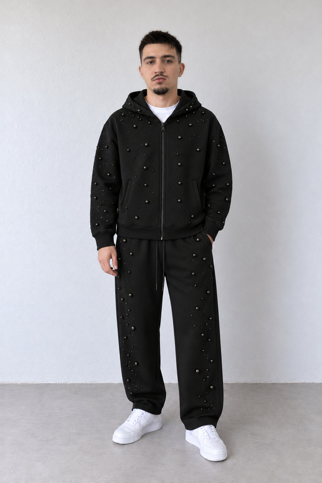 Trening negru pentru bărbați cu strasuri și mărgele decorative, ținută integrală pe model cu pantaloni asortați și sneakers albi.