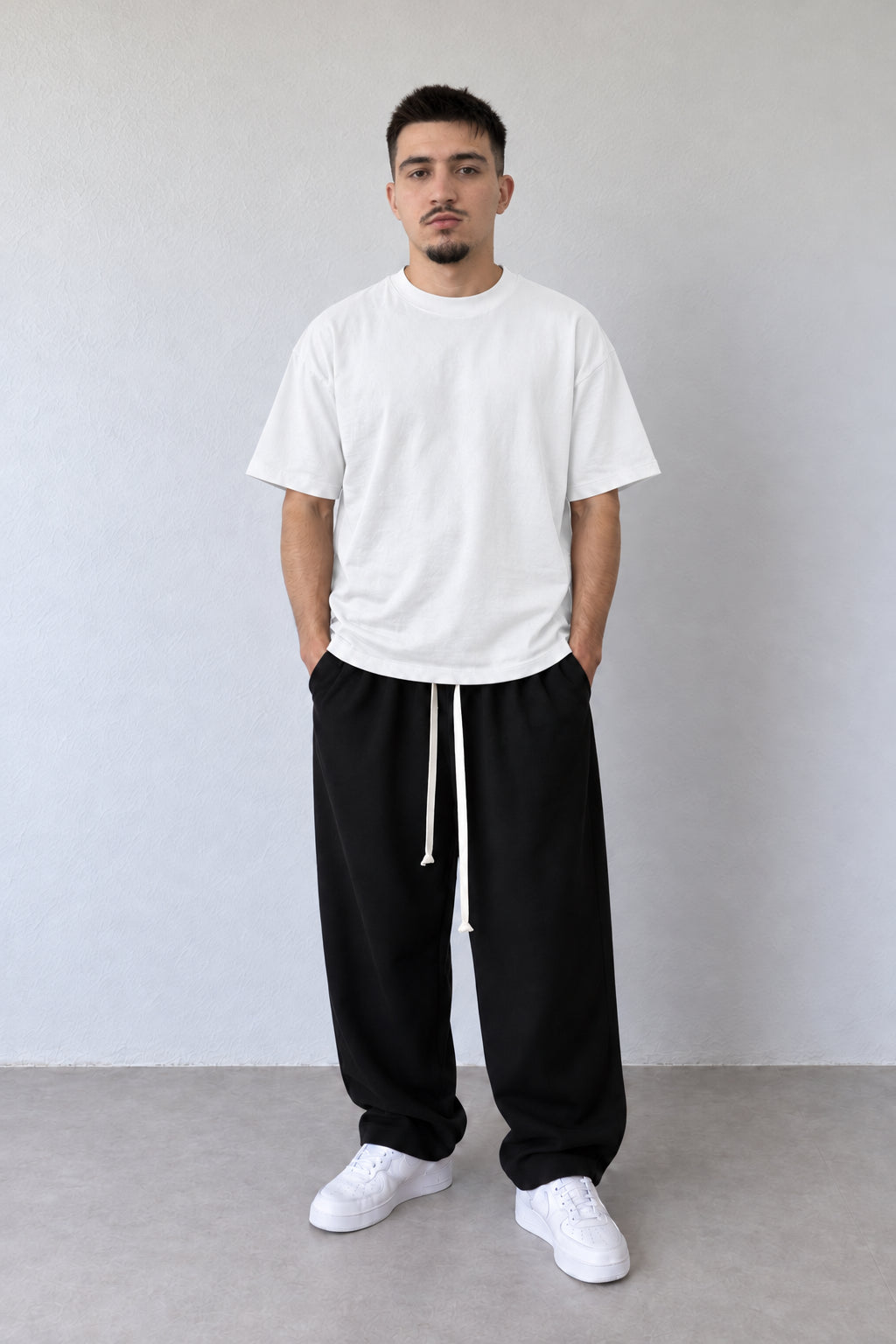 Tricou alb L815002 pentru bărbați, din bumbac cu croială lejeră și umeri căzuți, într-o ținută cu pantaloni negri.