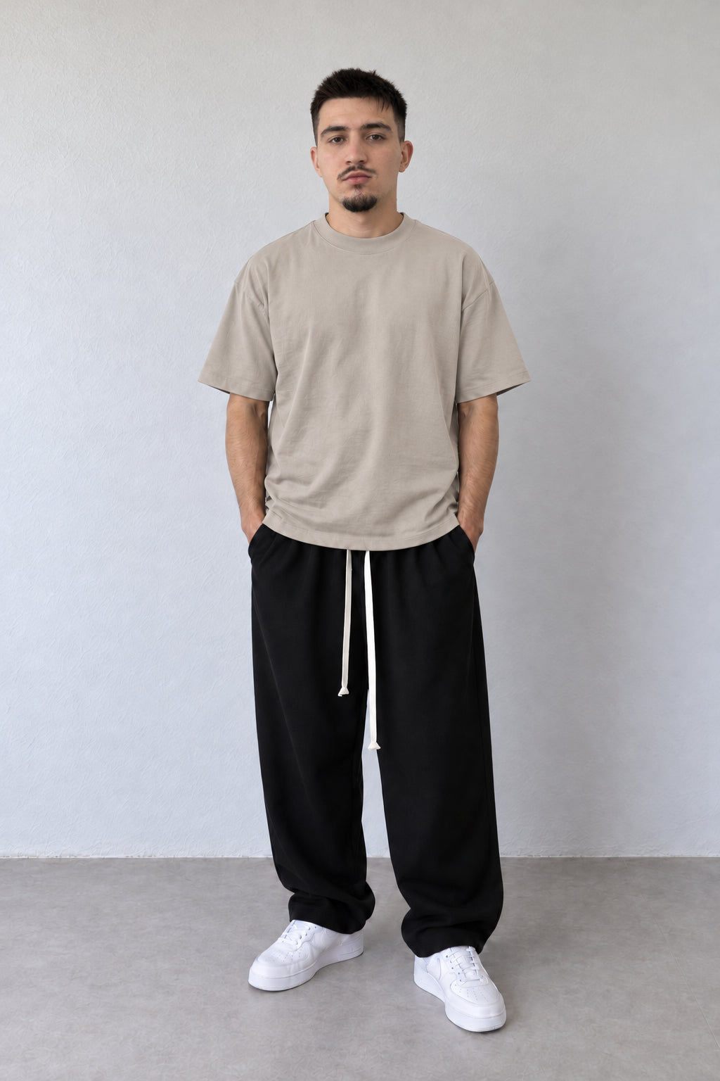 Tricou bej lejer L815002 din bumbac pentru bărbați, într-o ținută cu pantaloni negri largi și pantofi albi.