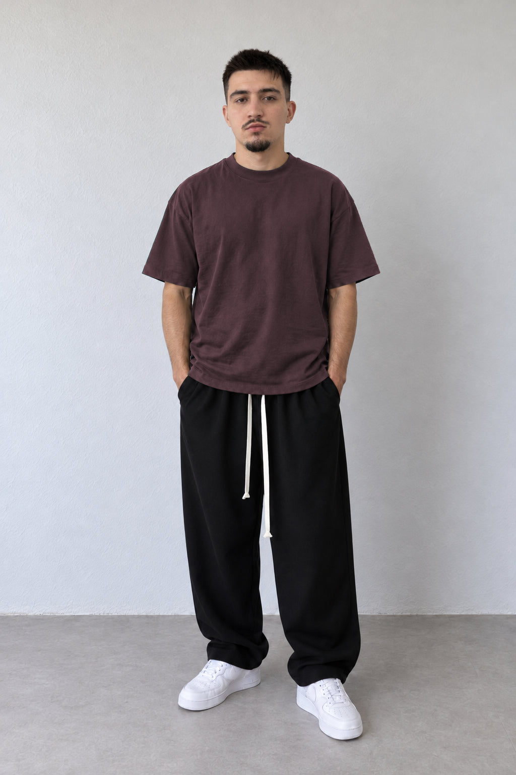 Tricou bordo L815002 pentru bărbați, din bumbac cu croială lejeră și umeri căzuți, purtat cu pantaloni negri.