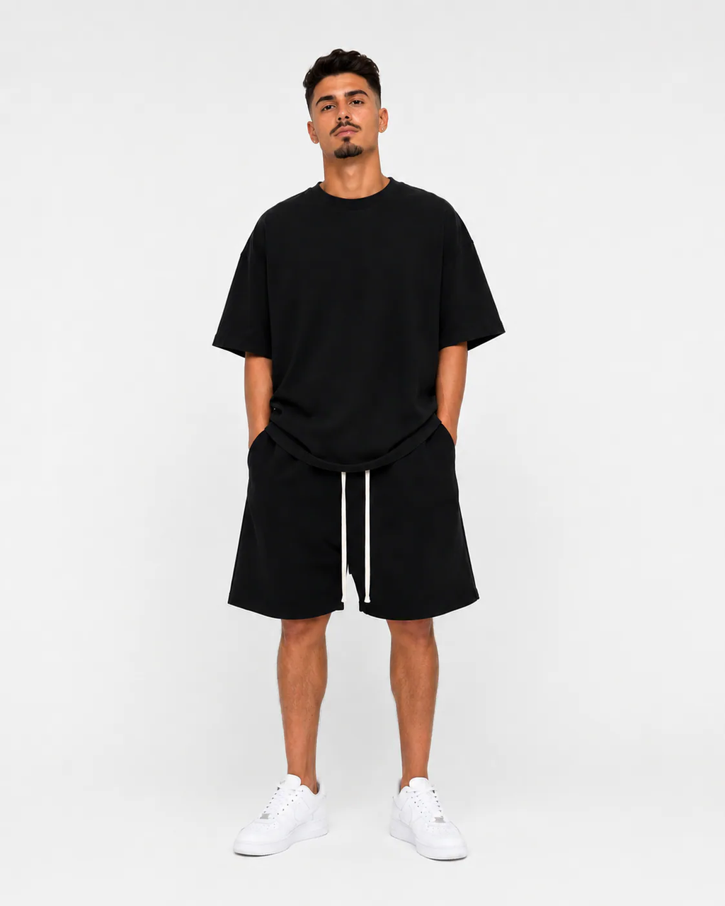 Model masculin purtând tricou oversized negru premium și pantaloni scurți largi streetwear într-un studio minimalist