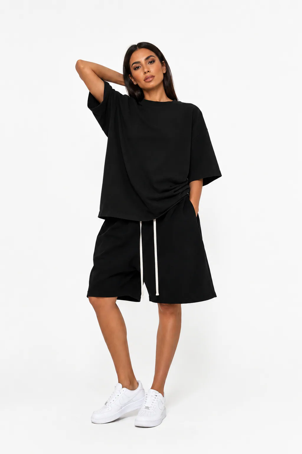 Model feminin purtând tricou oversized negru premium și pantaloni scurți largi streetwear într-un studio minimalist alb