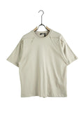 Model purtând un tricou unisex de culoare crem, realizat din 100% bumbac, cu o croială lejeră și un design minimalist accentuat de cusături decorative aparente.